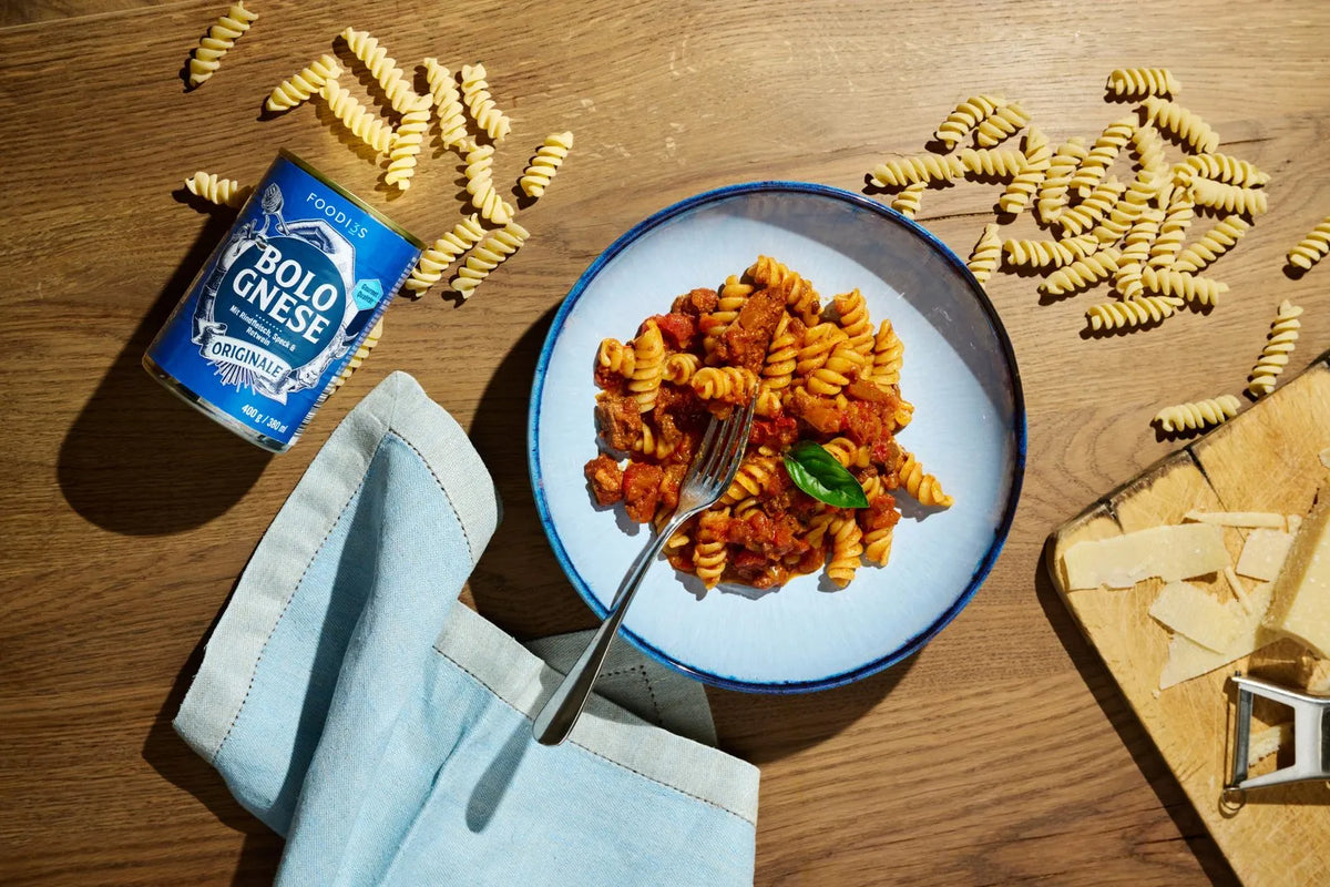 Eine Dose 3foodies Bolognese Originale neben einem Teller Fusilli mit Bolognese